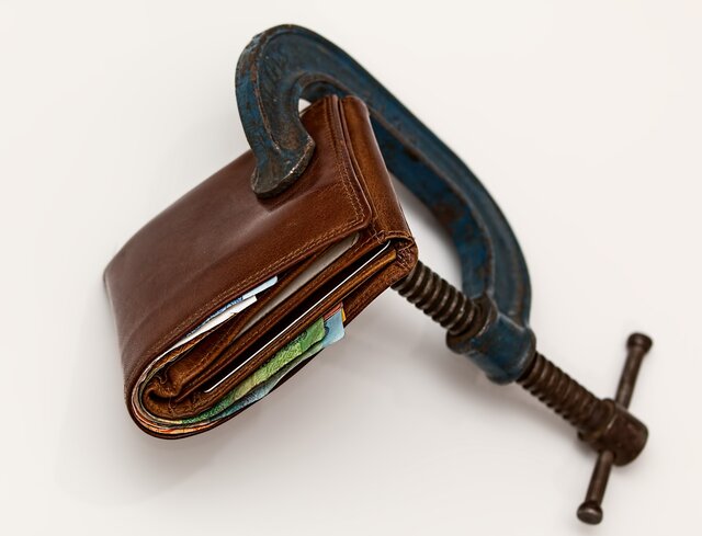 Braune Brieftasche mit herausragenden Geldscheinen in einer Zwinge fixiert.