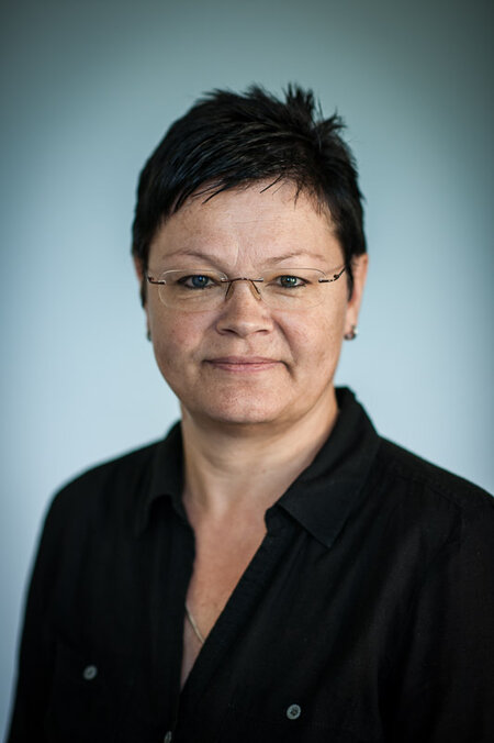 Person mit Brille und kurzem, dunklem Haar vor unscharfem, neutralem Hintergrund.