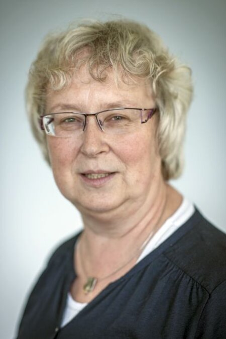 Person mit Brille und hellgrauen Haaren, blickt freundlich. Hintergrund unscharf.