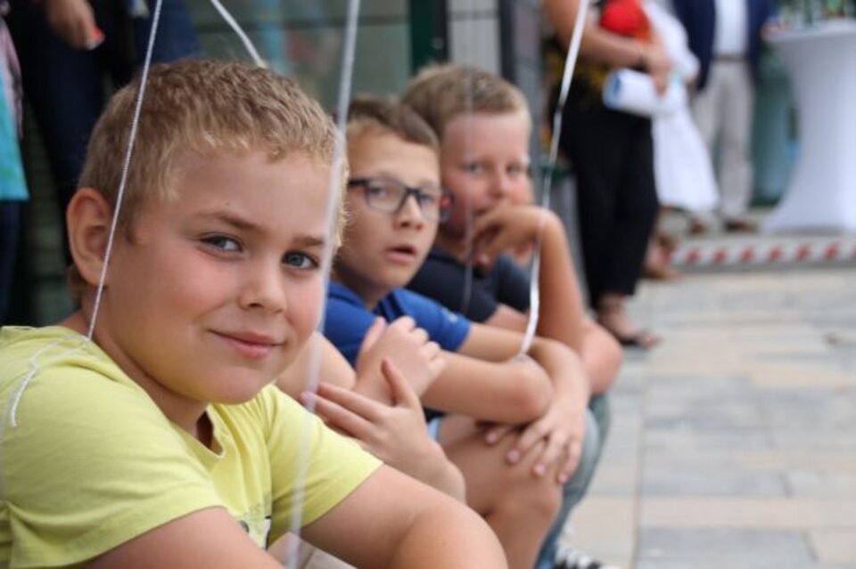 Vier Jungen sitzen in einer Reihe auf dem Boden, einige halten farbige Ballons.