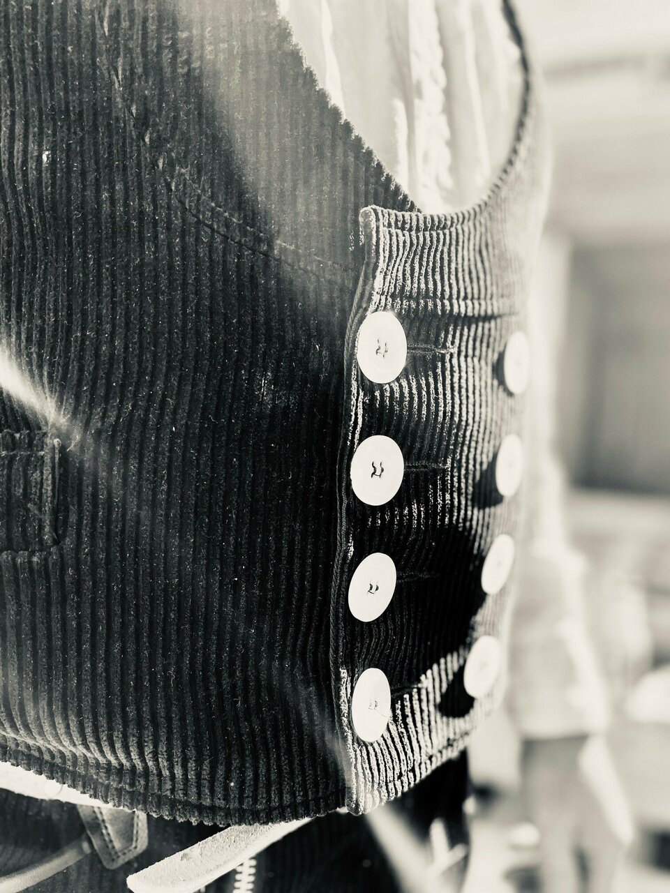 Detail einer dunklen Kordjacke mit acht weißen Knöpfen in Schwarz-Weiß.