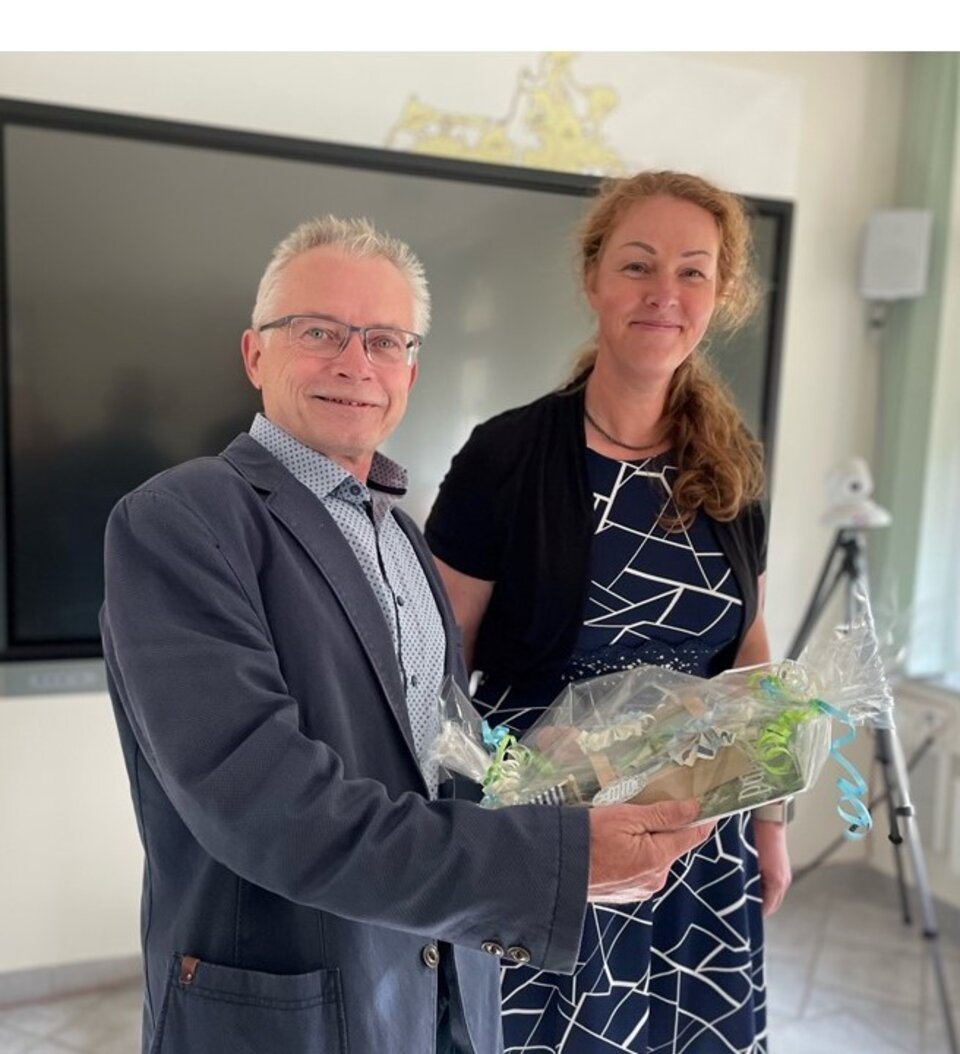 Mann und Frau halten gemeinsam ein Geschenk in einem Raum mit Bildschirm.