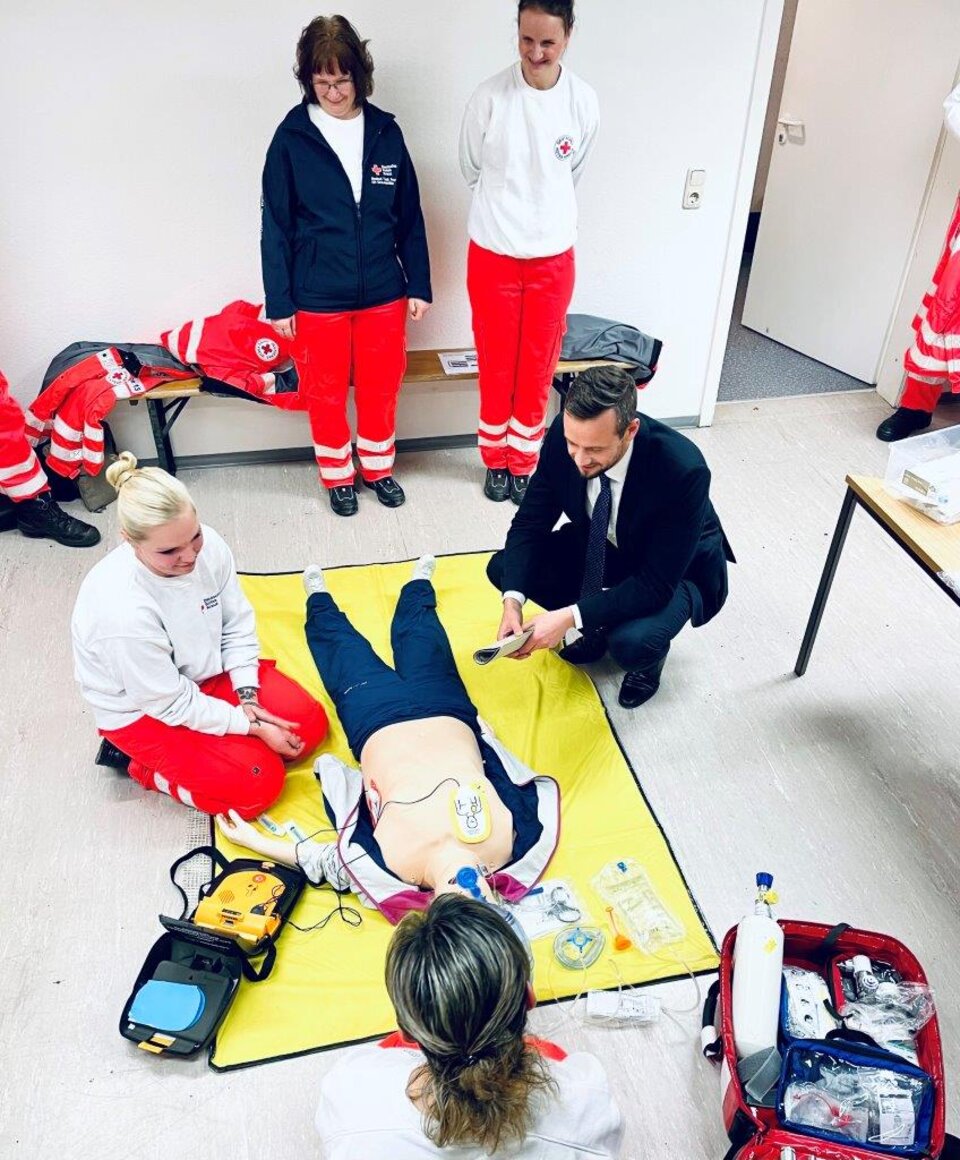 Trainingssituation zur Ersten Hilfe: Eine Puppe mit Defibrillator, umgeben von vier Menschen in Rettungsdienstbekleidung.