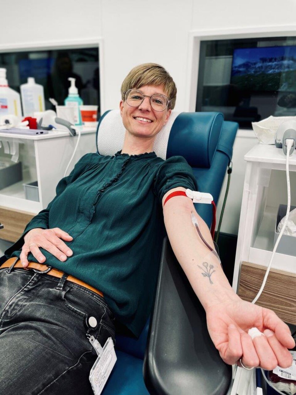 Person spendet Blut im Krankenhaus, sitzt auf einem Stuhl, entspannte Haltung, Tattoo auf dem Arm erkennbar.
