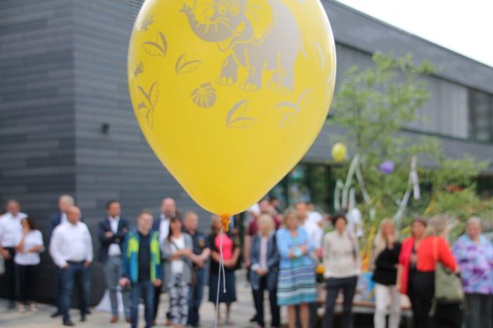 Gelber Ballon mit Elefantenmotiv, unscharfe Menschenmenge und modernes Gebäude im Hintergrund.