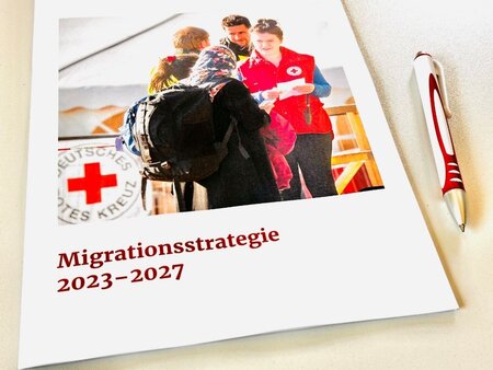 Mappe „Migrationsstrategie 2023–2027“ des Deutschen Roten Kreuzes auf Tisch mit Kugelschreiber.